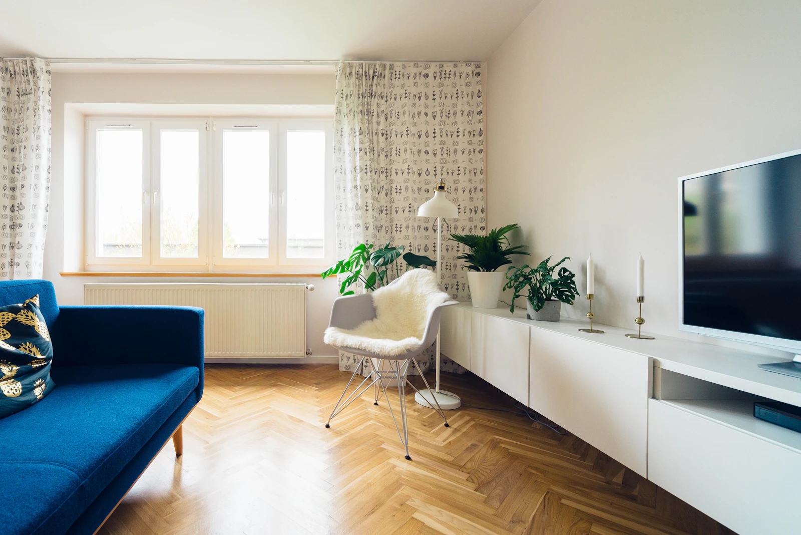 Sala com soalho em espinha, sofá azul e janela ampla