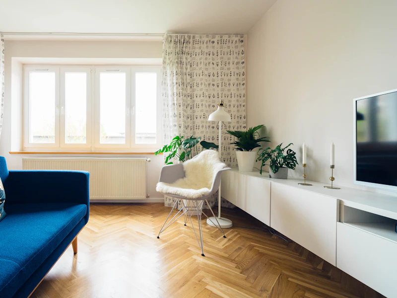 Sala com soalho em espinha, sofá azul e janela ampla