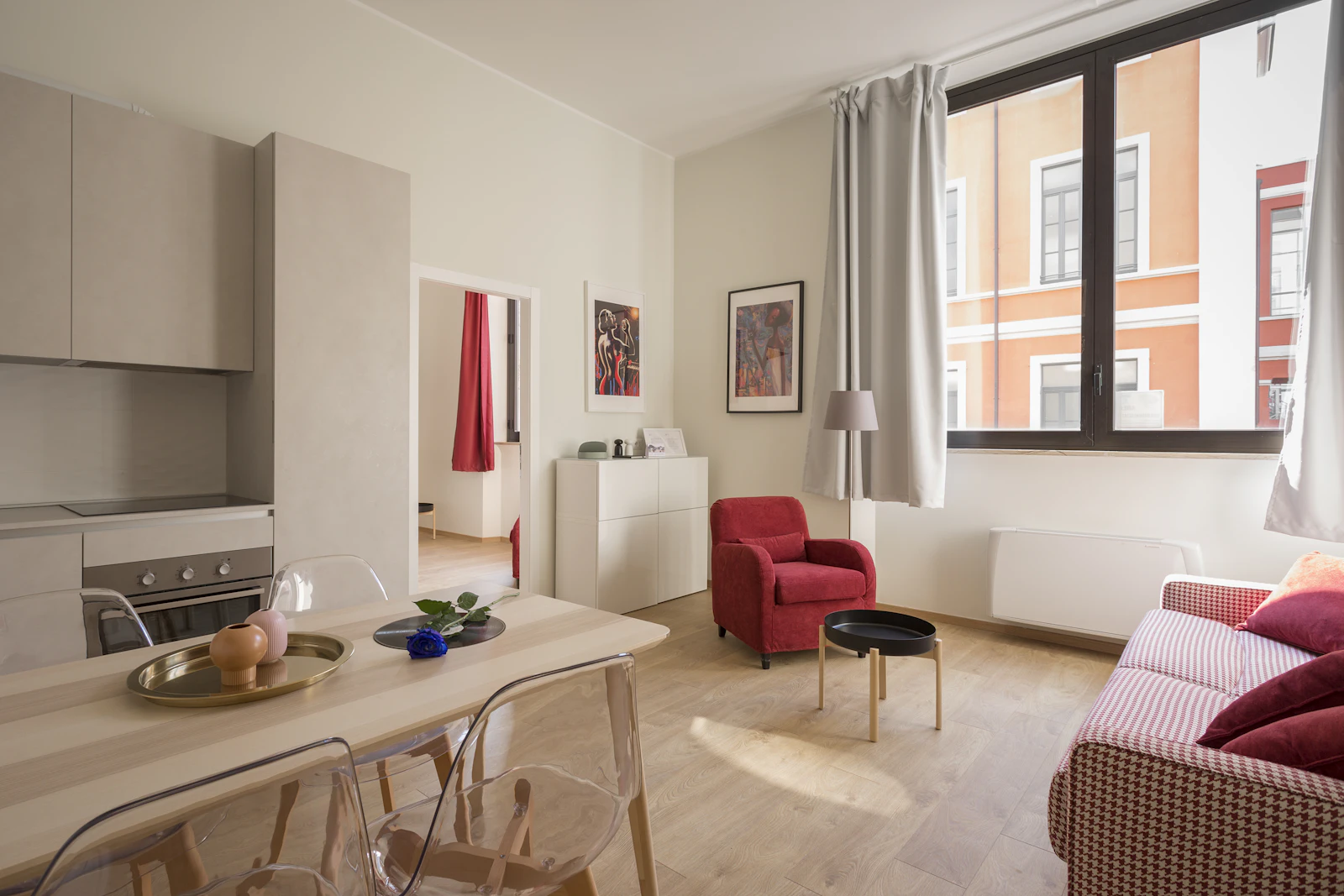 Sala com cadeirão vermelho, mesa de jantar e janela para a rua