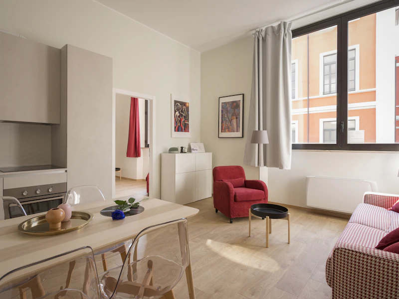 Sala com cadeirão vermelho, mesa de jantar e janela para a rua