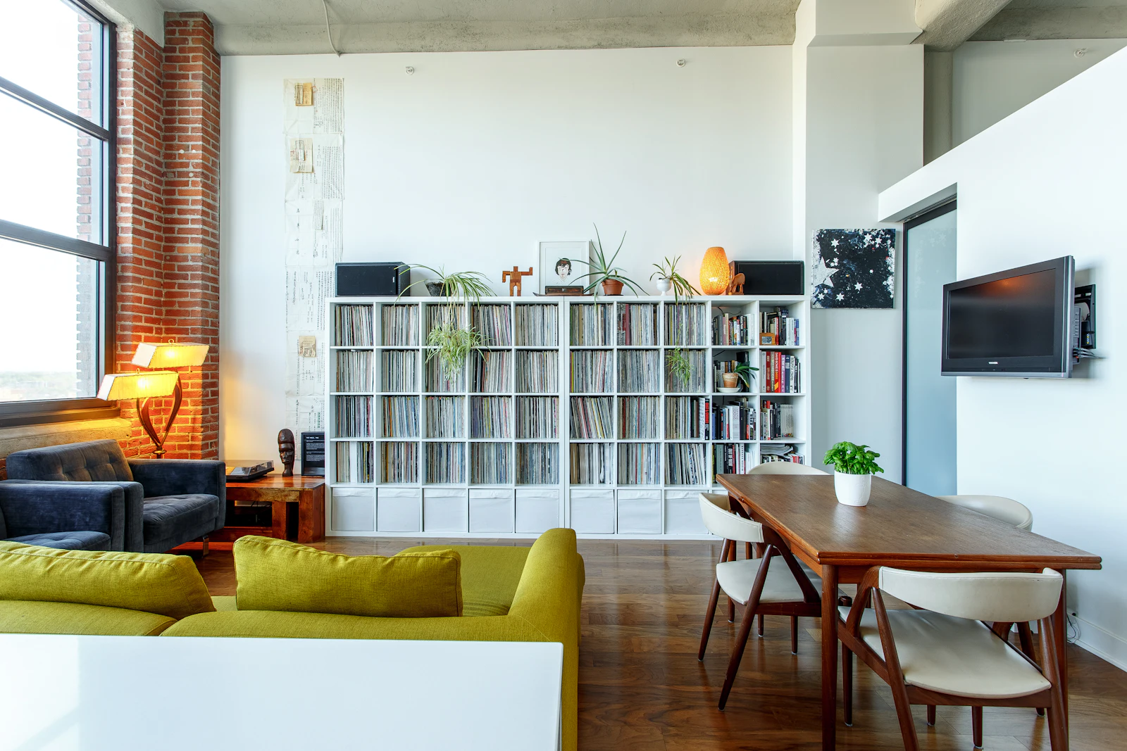 Loft com parede de tijolo, estante branca e sofá verde