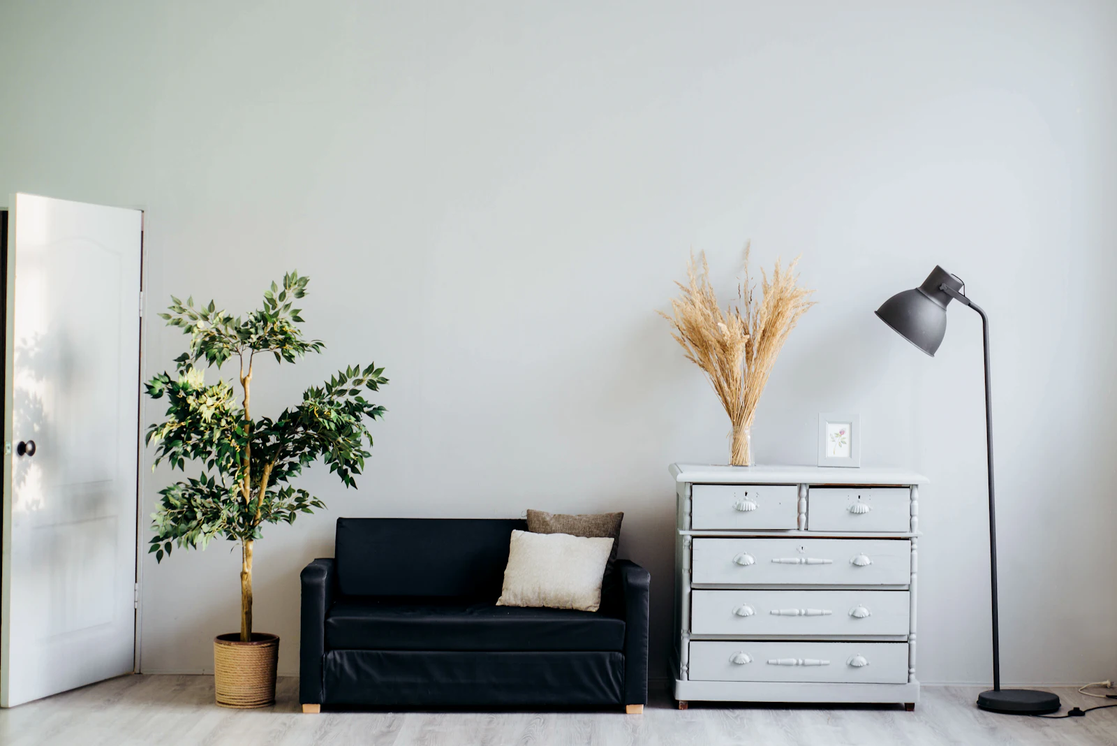 Estúdio minimalista com sofá preto, cómoda branca e planta